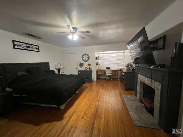 bedroom featuring a stone fireplace, ceiling fan, and hardwood / wood-style floors