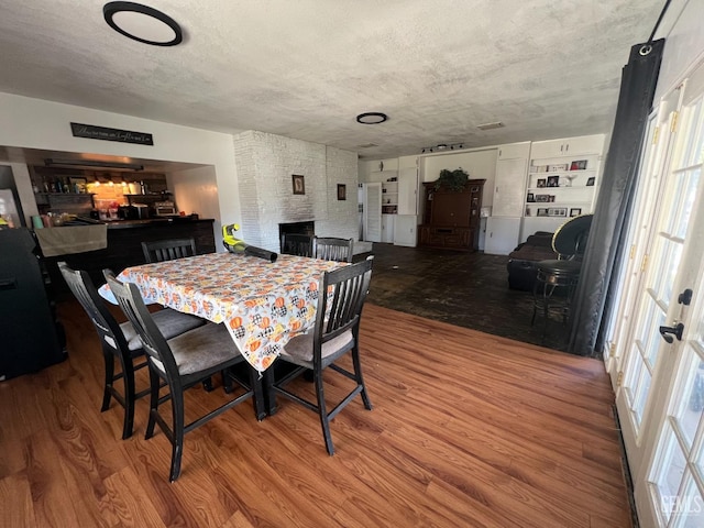 dining area featuring hardwood / wood-style flooring, a fireplace, and a textured ceiling