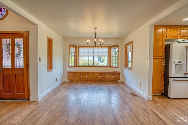 unfurnished dining area featuring light wood-type flooring and an inviting chandelier