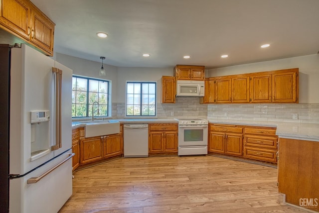 kitchen featuring backsplash, white appliances, sink, decorative light fixtures, and light hardwood / wood-style floors