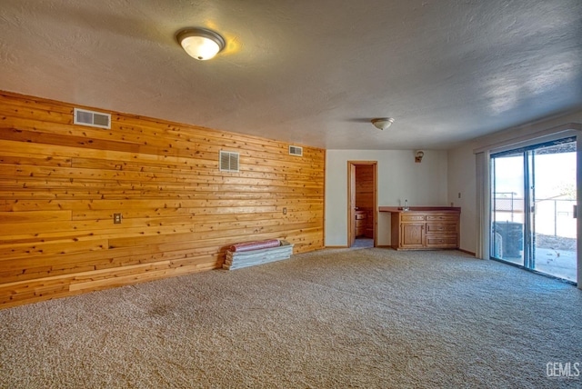 unfurnished living room featuring carpet, a textured ceiling, and wooden walls