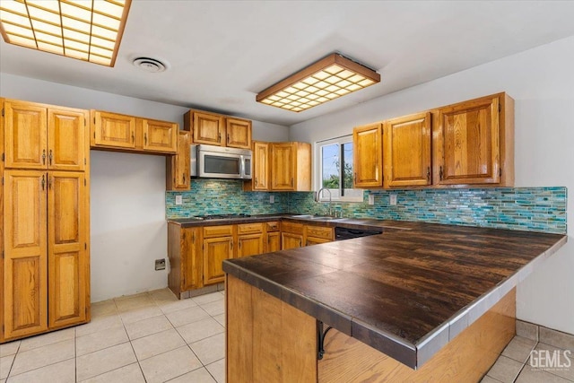 kitchen featuring brown cabinets, stainless steel appliances, dark countertops, a sink, and a peninsula