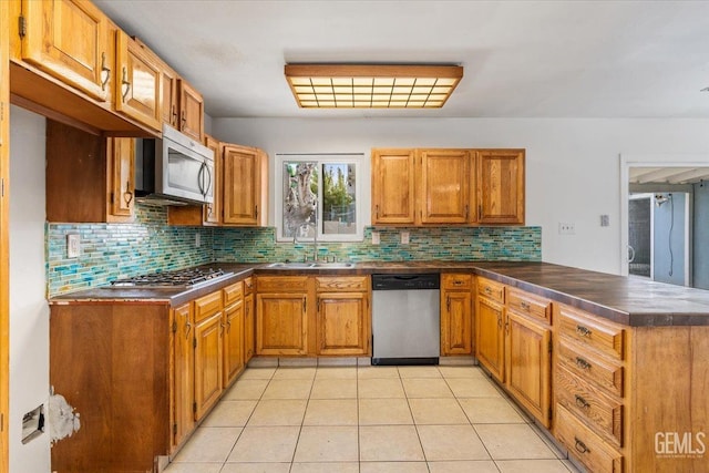 kitchen featuring a peninsula, appliances with stainless steel finishes, brown cabinetry, and a sink