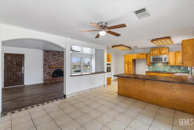 kitchen featuring visible vents, dark countertops, appliances with stainless steel finishes, a brick fireplace, and light tile patterned flooring