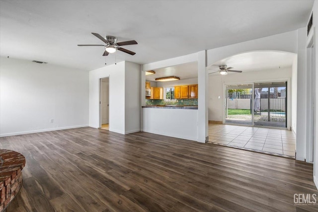 unfurnished living room featuring arched walkways, visible vents, dark wood finished floors, and ceiling fan