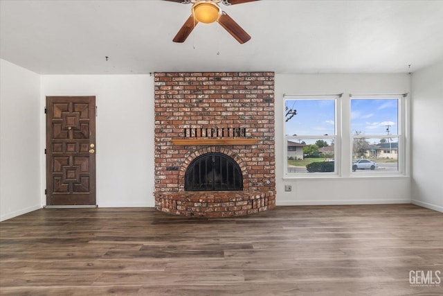 unfurnished living room with a brick fireplace, ceiling fan, baseboards, and wood finished floors