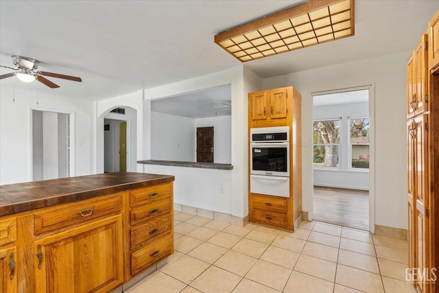 kitchen with arched walkways, a warming drawer, dark countertops, ceiling fan, and oven