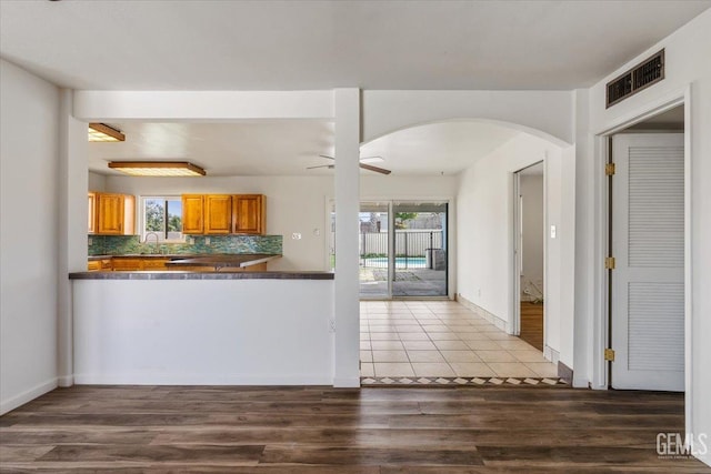 kitchen featuring wood finished floors, a ceiling fan, visible vents, decorative backsplash, and dark countertops