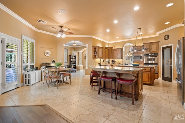 2801 Trengate Way, Bakersfield, CA 93311 - kitchen with appliances with stainless steel finishes, ornamental molding, arched walkways, brown cabinets, and light stone countertops