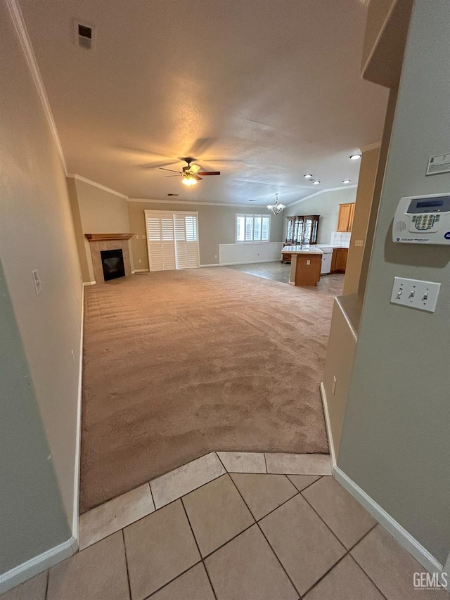 unfurnished living room with crown molding, a fireplace, ceiling fan with notable chandelier, and carpet floors
