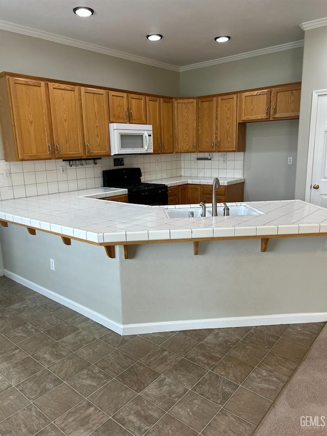 kitchen featuring black gas range, tile countertops, kitchen peninsula, and a kitchen bar