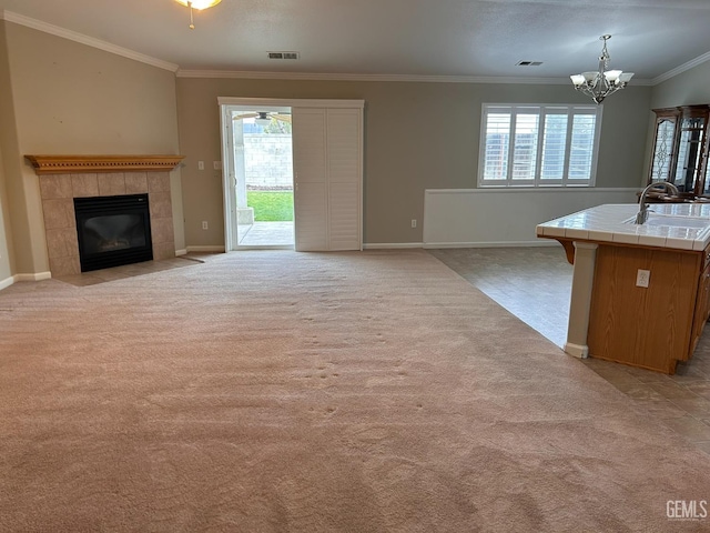 unfurnished living room featuring a tile fireplace, sink, a chandelier, light colored carpet, and crown molding