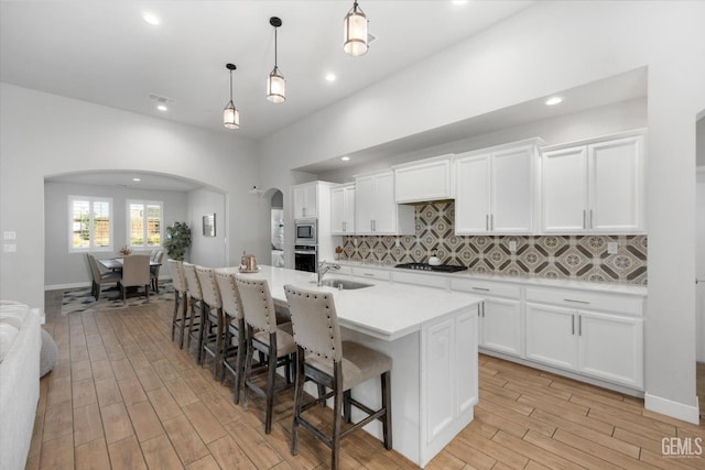 kitchen featuring backsplash, a center island with sink, appliances with stainless steel finishes, decorative light fixtures, and white cabinetry