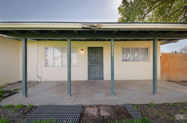 property entrance featuring a patio area, fence, and stucco siding