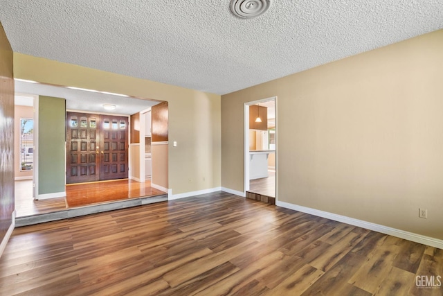 unfurnished living room with a textured ceiling, wood finished floors, and baseboards