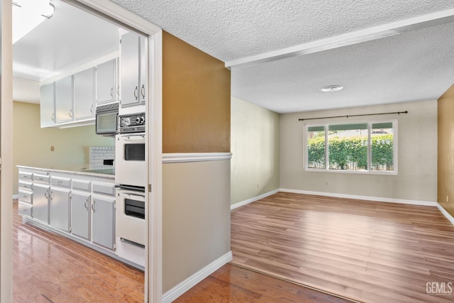 kitchen featuring double oven, light wood finished floors, baseboards, a textured ceiling, and light countertops