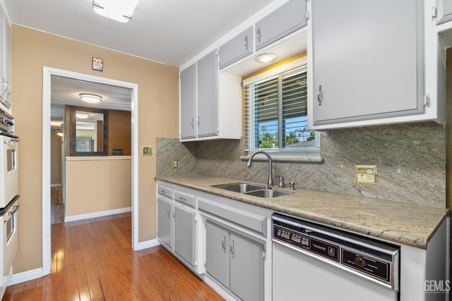 kitchen with white dishwasher, a sink, baseboards, light wood-style flooring, and backsplash