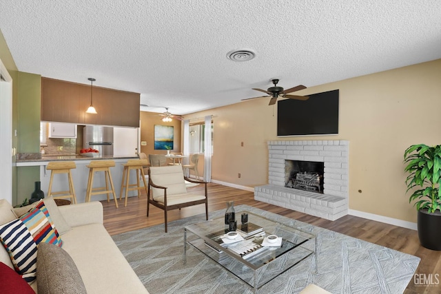 living area featuring ceiling fan, light wood-type flooring, a textured ceiling, a fireplace, and baseboards