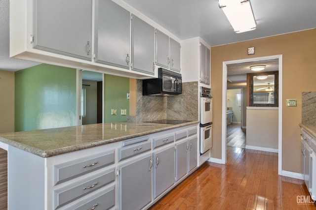 kitchen featuring black appliances, baseboards, light wood-style floors, gray cabinetry, and a peninsula