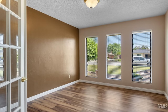 unfurnished room featuring wood finished floors, a textured ceiling, and baseboards