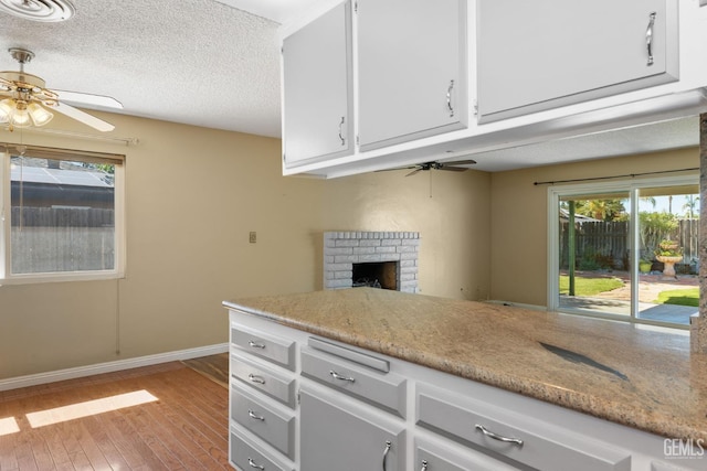 kitchen featuring ceiling fan, light wood-style floors, white cabinetry, a brick fireplace, and a textured ceiling