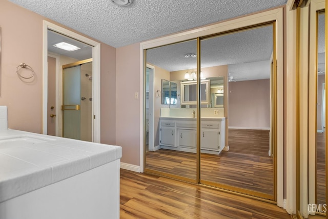 bedroom with a textured ceiling, wood finished floors, a sink, baseboards, and a closet