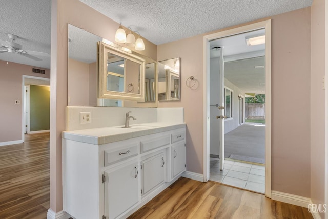 bathroom with wood finished floors, a textured ceiling, baseboards, a ceiling fan, and vanity