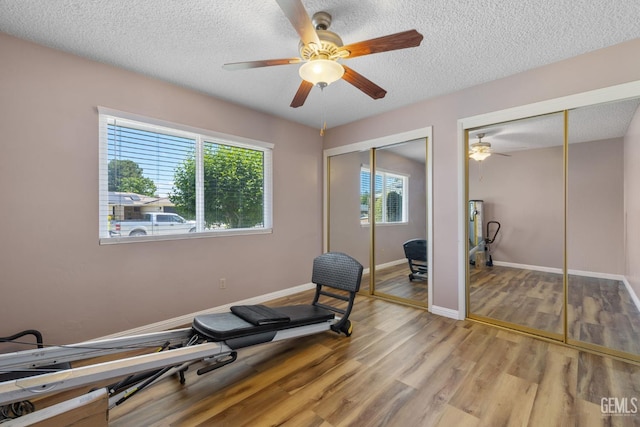 workout room with light wood-style floors, ceiling fan, a textured ceiling, and baseboards