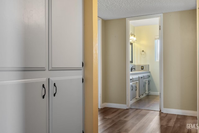 hallway featuring wood finished floors, a textured ceiling, baseboards, and a sink