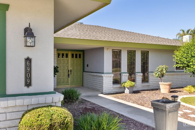 entrance to property featuring a shingled roof and stucco siding