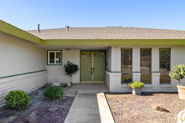 entrance to property featuring a shingled roof and stucco siding
