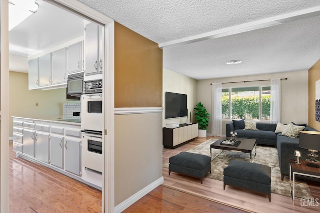 living room featuring light wood-style floors, a textured ceiling, and baseboards