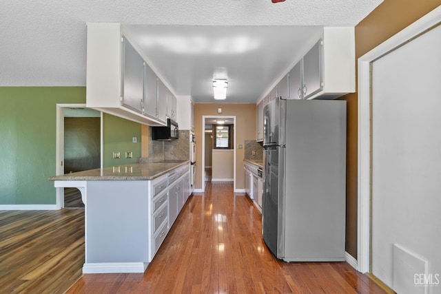 kitchen featuring black appliances, wood finished floors, baseboards, and backsplash