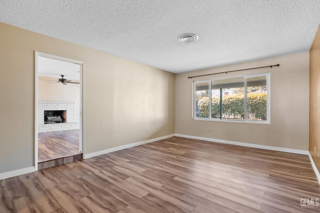 empty room featuring wood finished floors, a textured ceiling, a fireplace, a ceiling fan, and baseboards