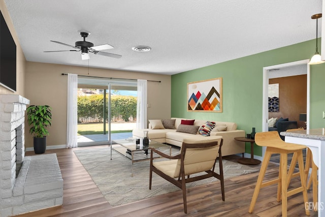 living area with ceiling fan, wood finished floors, baseboards, a fireplace, and a textured ceiling