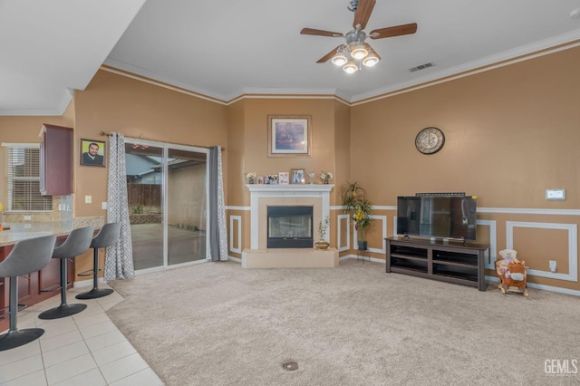 tiled living room featuring ceiling fan, crown molding, and a tile fireplace