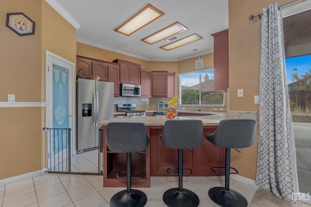 kitchen with kitchen peninsula, ornamental molding, a breakfast bar, stainless steel appliances, and light tile patterned flooring