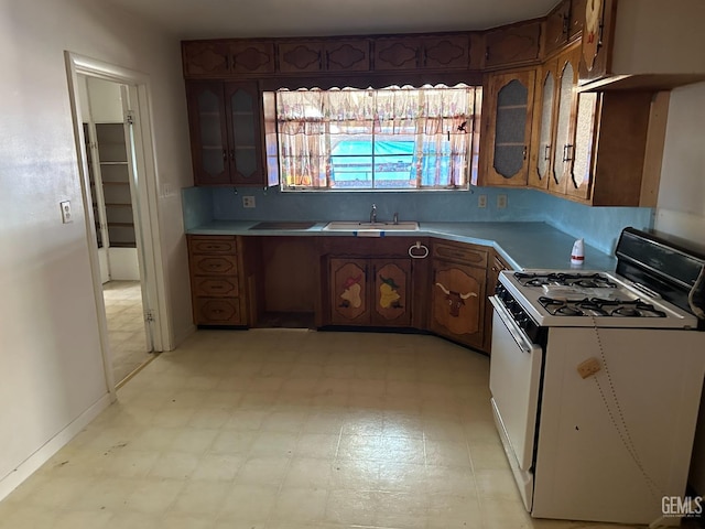 kitchen featuring a sink, gas range gas stove, light countertops, glass insert cabinets, and light floors