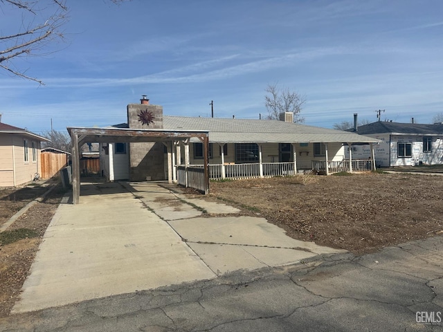 view of front of property with fence, concrete driveway, covered porch, a chimney, and a carport