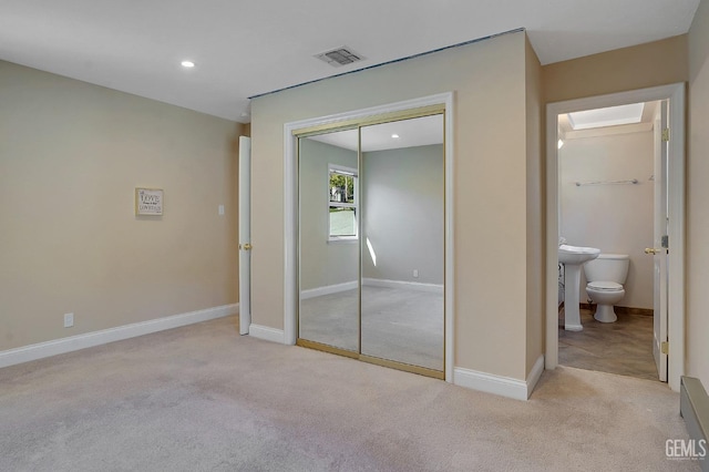 unfurnished bedroom with light carpet, ensuite bathroom, and a closet