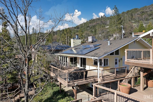 rear view of property featuring solar panels and a wooden deck