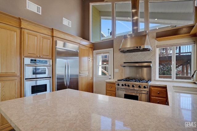 kitchen with a healthy amount of sunlight, high quality appliances, wall chimney range hood, and sink