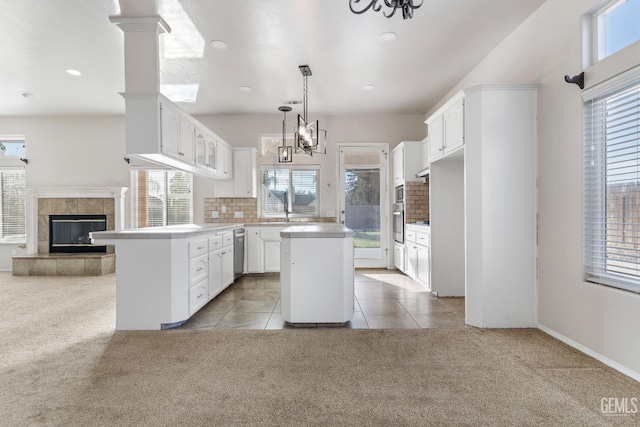 kitchen featuring light carpet, a kitchen island, white cabinets, decorative backsplash, and a tiled fireplace