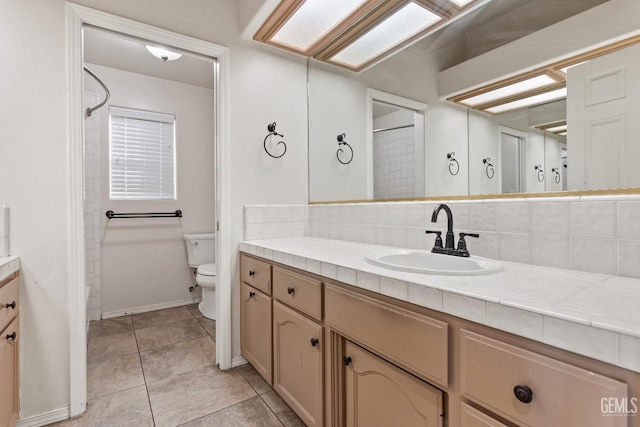 full bathroom featuring toilet, a skylight, vanity, decorative backsplash, and tile patterned floors