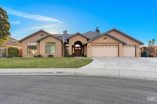 ranch-style home featuring a front yard, concrete driveway, fence, roof mounted solar panels, and stucco siding