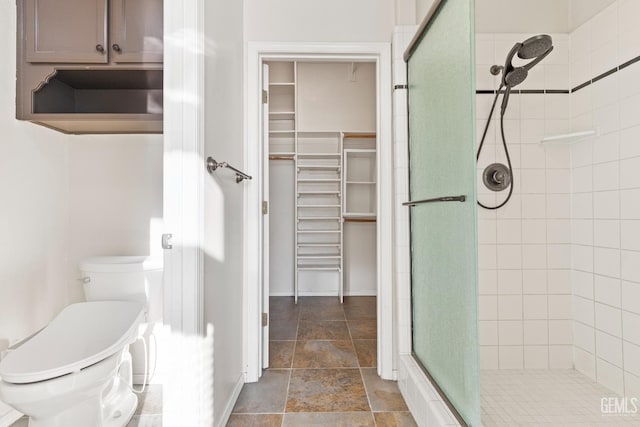 full bathroom with stone finish floor, a shower stall, toilet, and a walk in closet