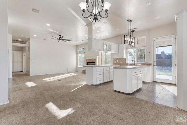 kitchen with light carpet, a kitchen island, white cabinetry, backsplash, and ceiling fan with notable chandelier