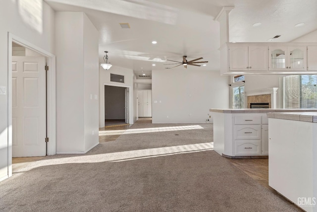 kitchen featuring ceiling fan, recessed lighting, light colored carpet, a fireplace, and white cabinets