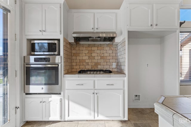 kitchen with appliances with stainless steel finishes, backsplash, white cabinets, and under cabinet range hood