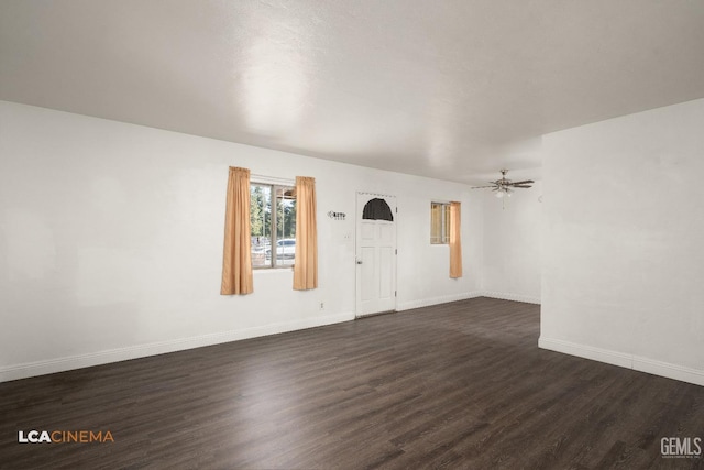 unfurnished living room with dark wood-style flooring, baseboards, and a ceiling fan